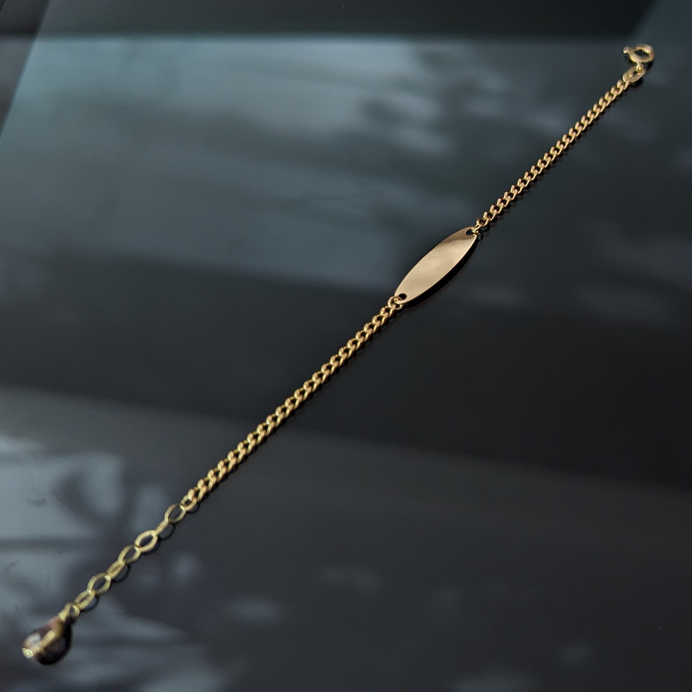 14K gold baby ID bracelet for girls with a blank nameplate and pink gemstone charm, displayed on a black background