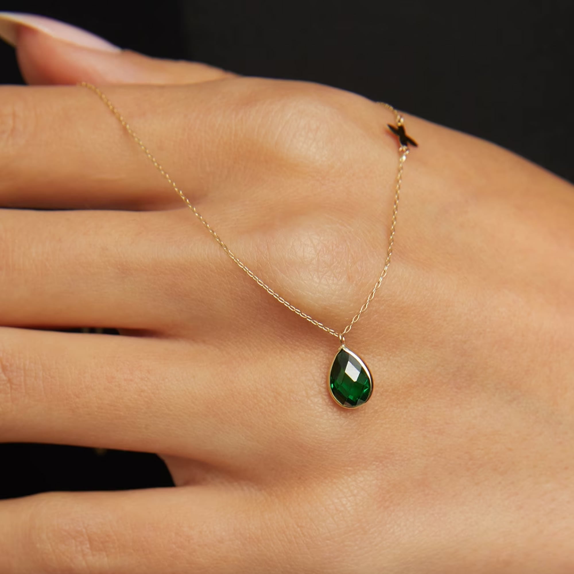 14K gold necklace with emerald teardrop pendant and butterfly charm worn on model’s neck