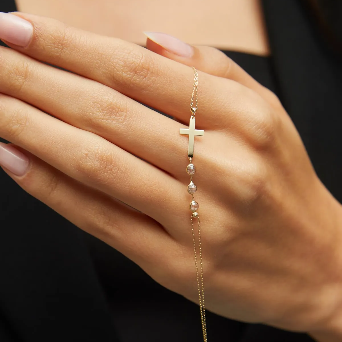 14K gold bracelet with minimalist cross and three small crystal beads, displayed on dark green satin fabric