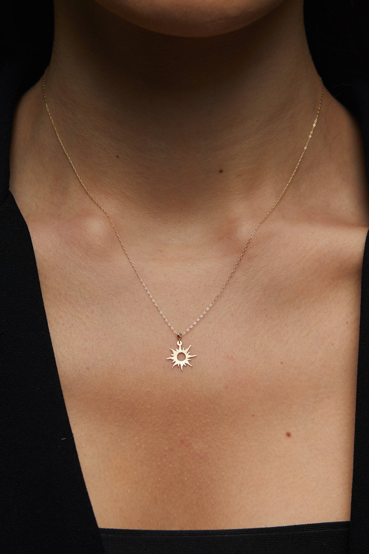 14K gold necklace featuring a radiant sunburst charm with pointed rays and a hollow center,