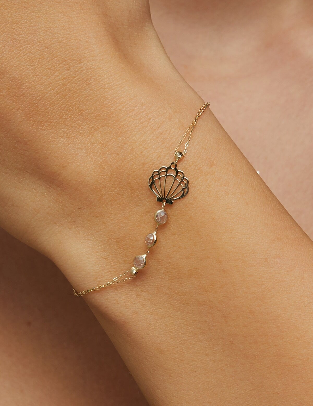 Elegant 14K gold bracelet with a cut-out seashell charm and faceted crystal beads, styled on rich emerald satin