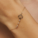 Elegant 14K gold bracelet with a cut-out seashell charm and faceted crystal beads, styled on rich emerald satin