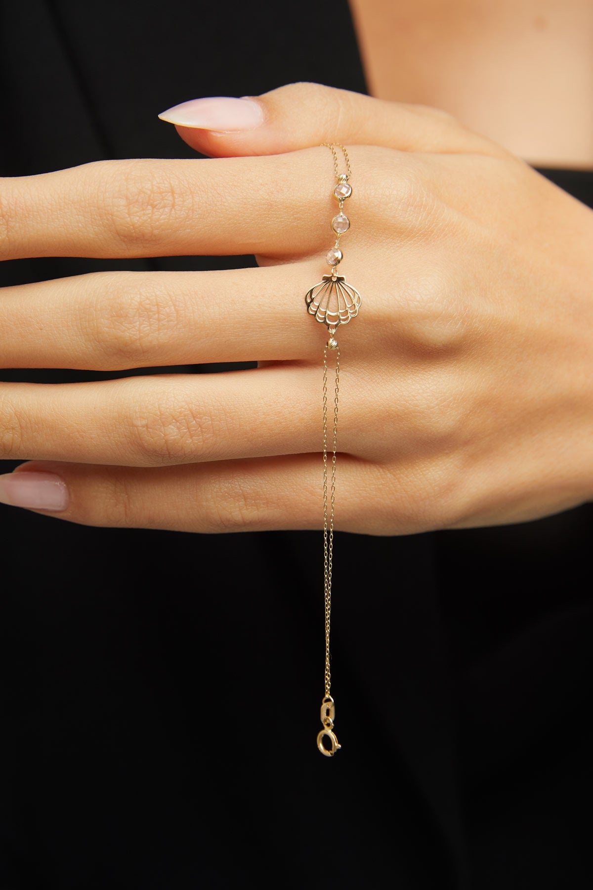 Elegant 14K gold bracelet with a cut-out seashell charm and faceted crystal beads, styled on rich emerald satin