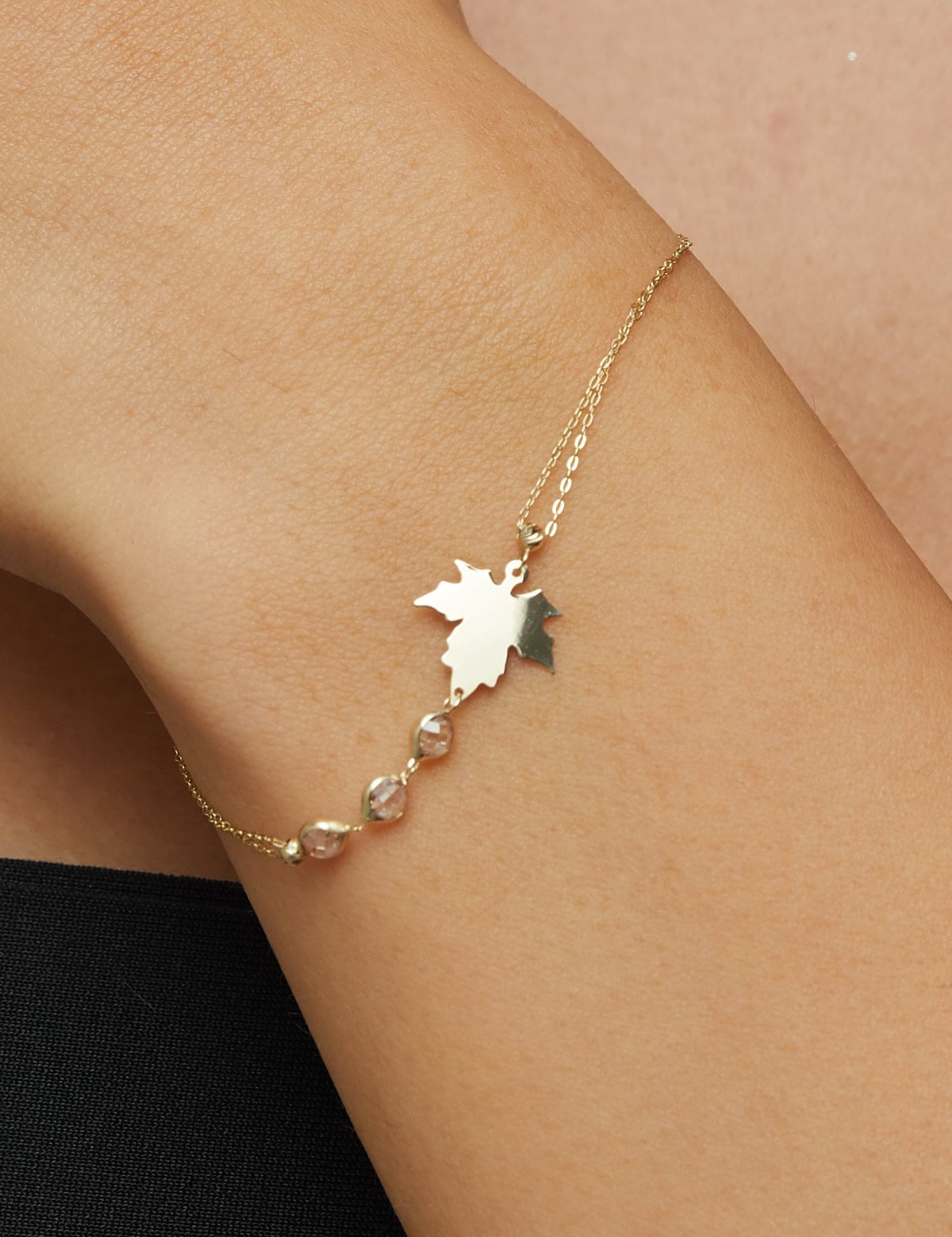 14K gold bracelet with maple leaf charm and gemstone accents on green satin