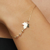 14K gold bracelet with maple leaf charm and gemstone accents on green satin