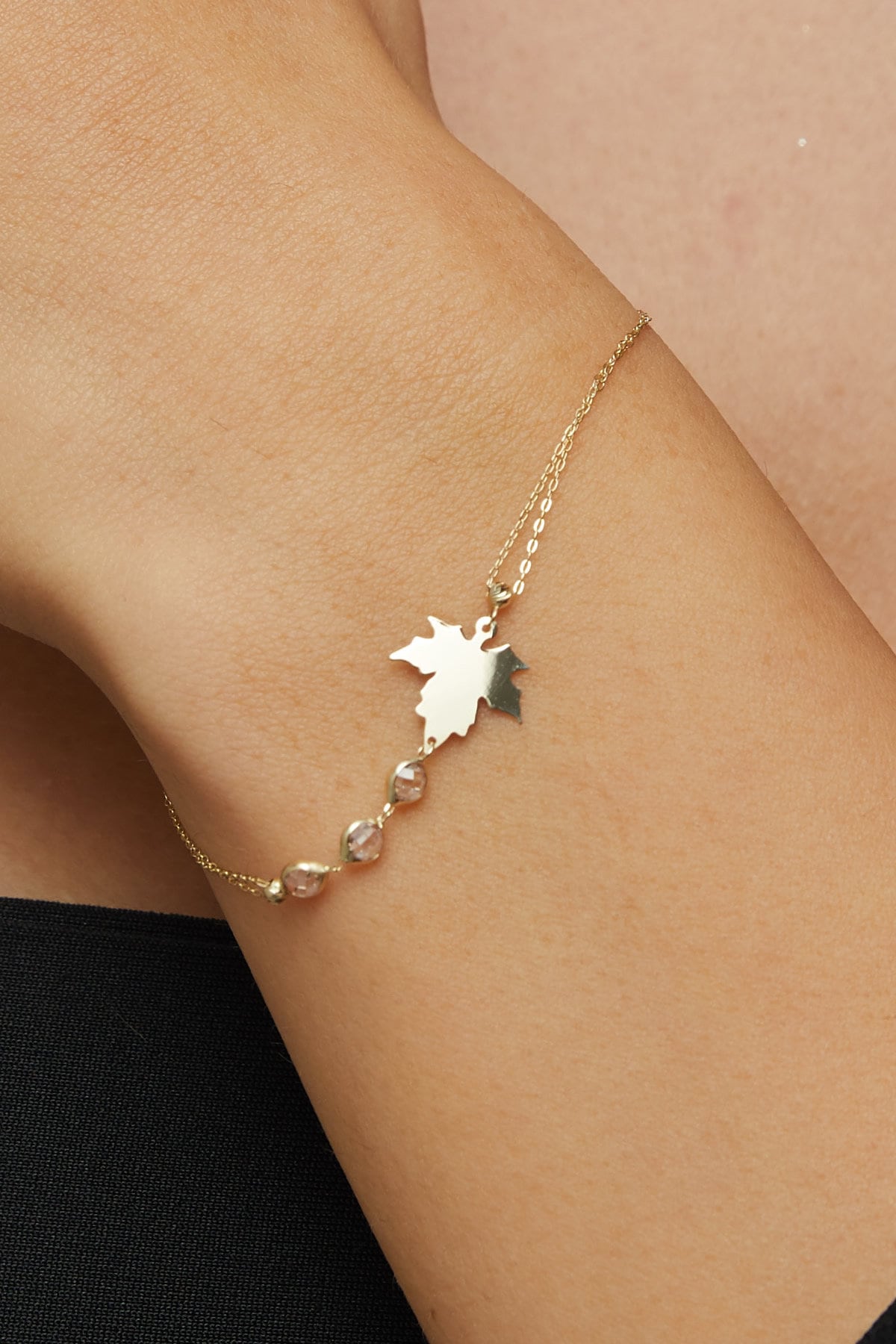 14K gold bracelet with maple leaf charm and gemstone accents on green satin