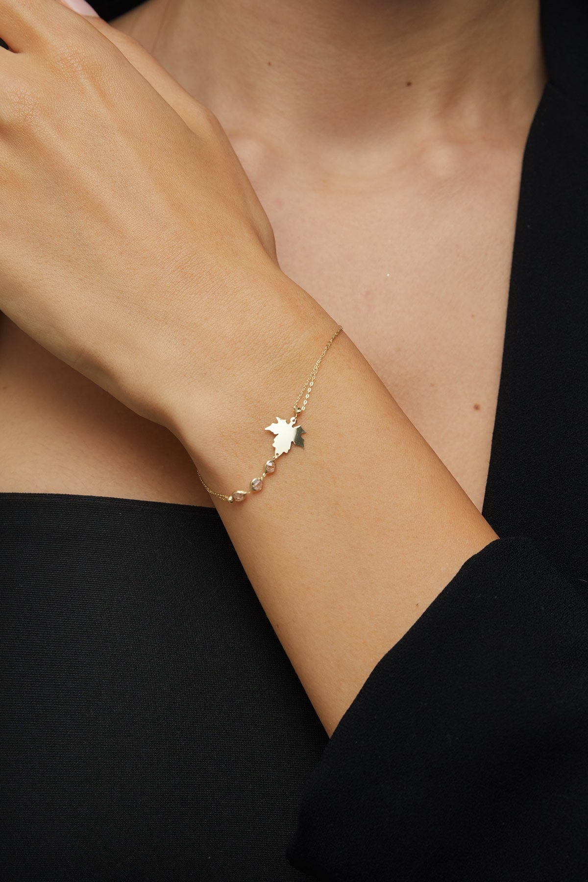 14K gold bracelet with maple leaf charm and gemstone accents on green satin