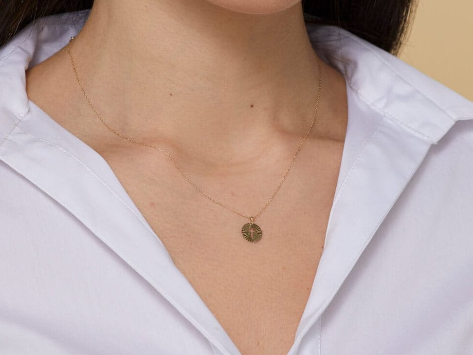 Minimalist 14K gold medallion necklace with a central cutout cross and radiant sunbeam engravings