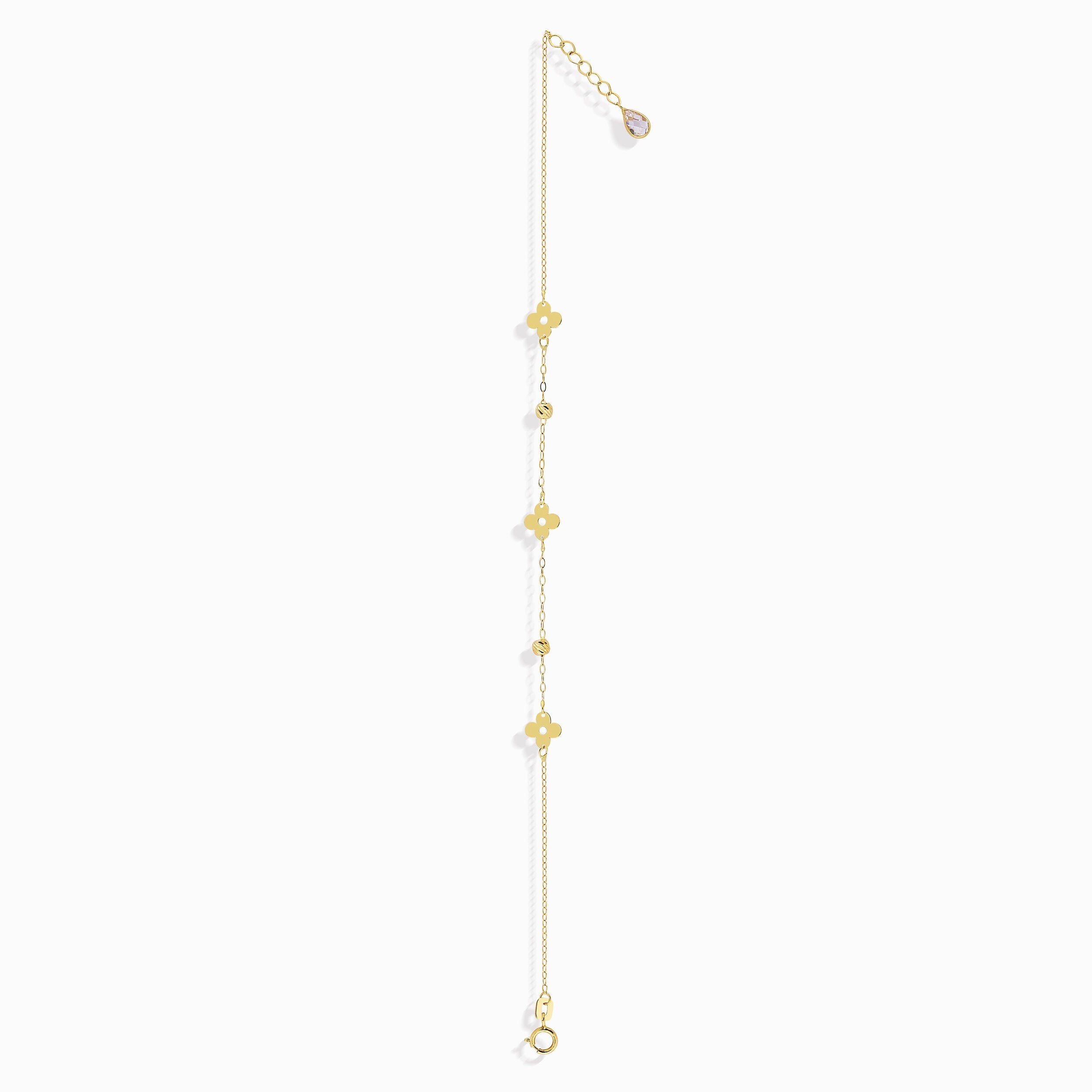 Minimalist 14K gold bracelet with clover-shaped charms and tiny textured accents, styled on emerald green silk fabric