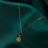 14K gold four leaf clover necklace with circular loop detail, styled on deep green satin background – elegant and symbolic.