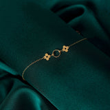 14K gold bracelet with a twisted circle centerpiece and two solid clover charms on a fine chain, displayed on deep green satin fabric.
