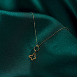 Minimal 14K gold necklace featuring a four-leaf clover charm hanging from a twisted circle, displayed on emerald green satin fabric.