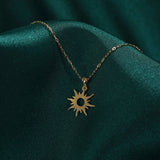 14K gold necklace featuring a radiant sunburst charm with pointed rays and a hollow center, styled on rich emerald green satin.