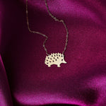 Close-up of a 14K gold hedgehog pendant necklace displayed on rich pink satin fabric.