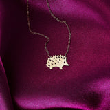 Close-up of a 14K gold hedgehog pendant necklace displayed on rich pink satin fabric.