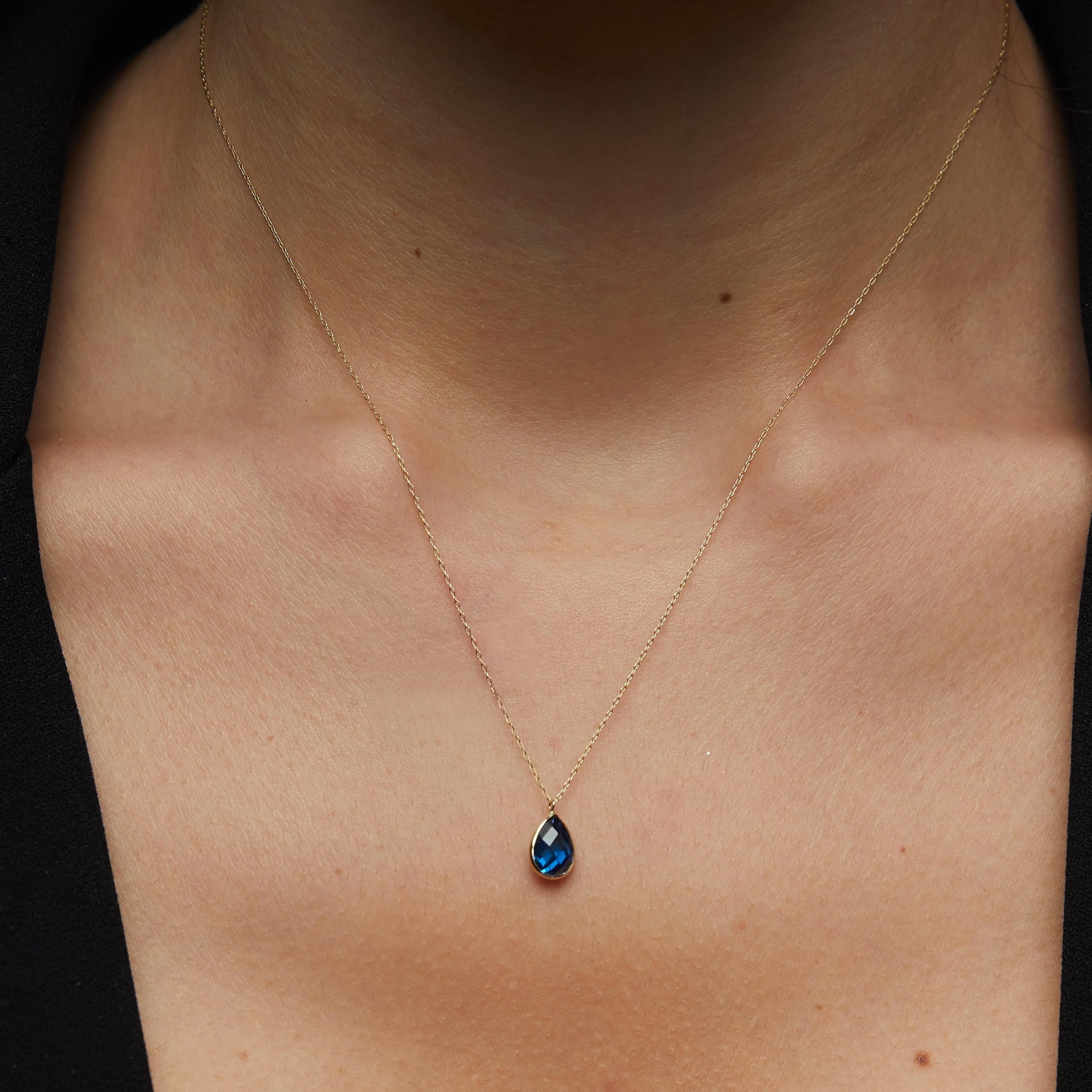 14K gold necklace with a faceted blue teardrop gemstone pendant resting on women