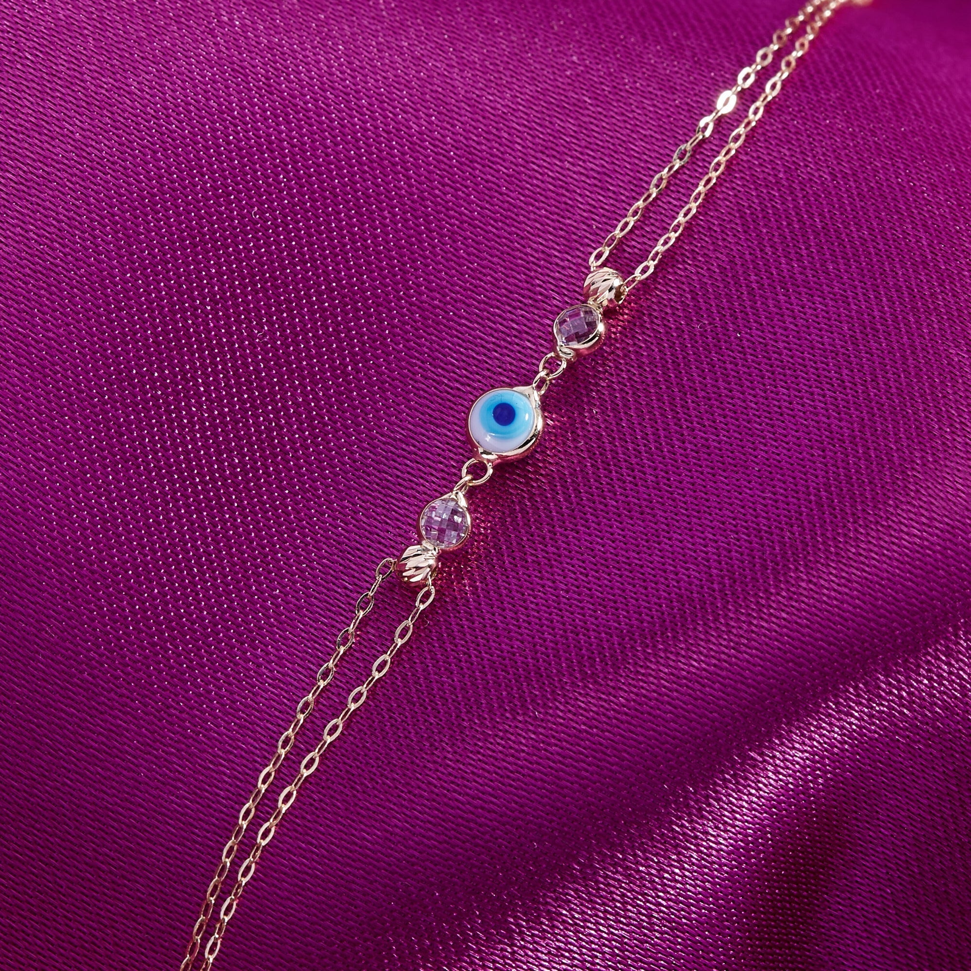 blue 14K gold evil eye bracelets with colorful charms and gemstone accents on pink background