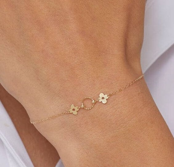 14K gold bracelet with a twisted circle centerpiece and two solid clover charms on a fine chain