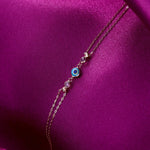 navy blue 14K gold evil eye bracelets with colorful charms and gemstone accents on pink background