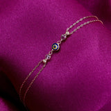 dark blue 14K gold evil eye bracelets with colorful charms and gemstone accents on pink background