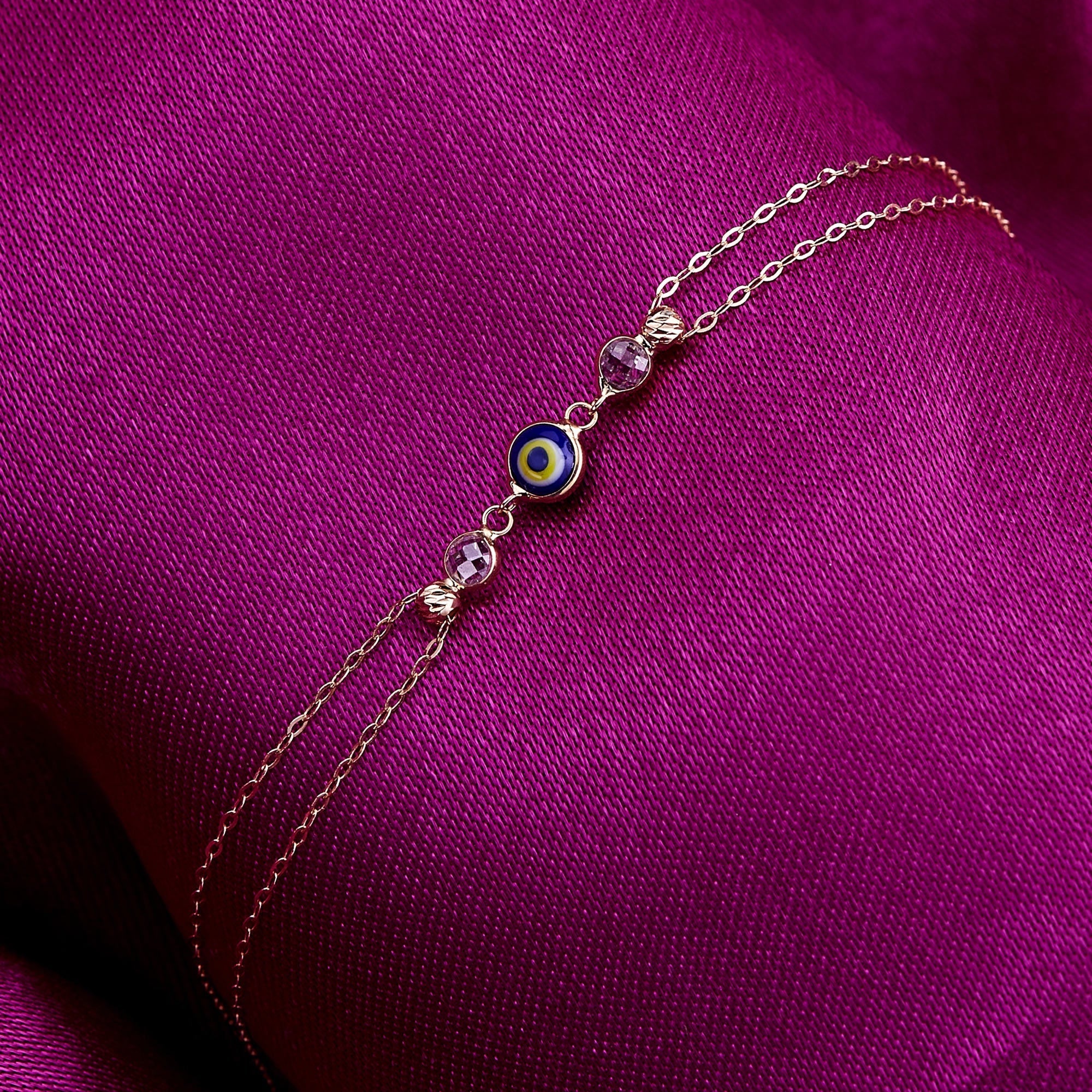 dark blue 14K gold evil eye bracelets with colorful charms and gemstone accents on pink background