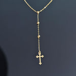 Close-up image of a 14K gold rosary-style necklace with a delicate cross pendant