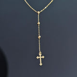 Close-up image of a 14K gold rosary-style necklace with a delicate cross pendant