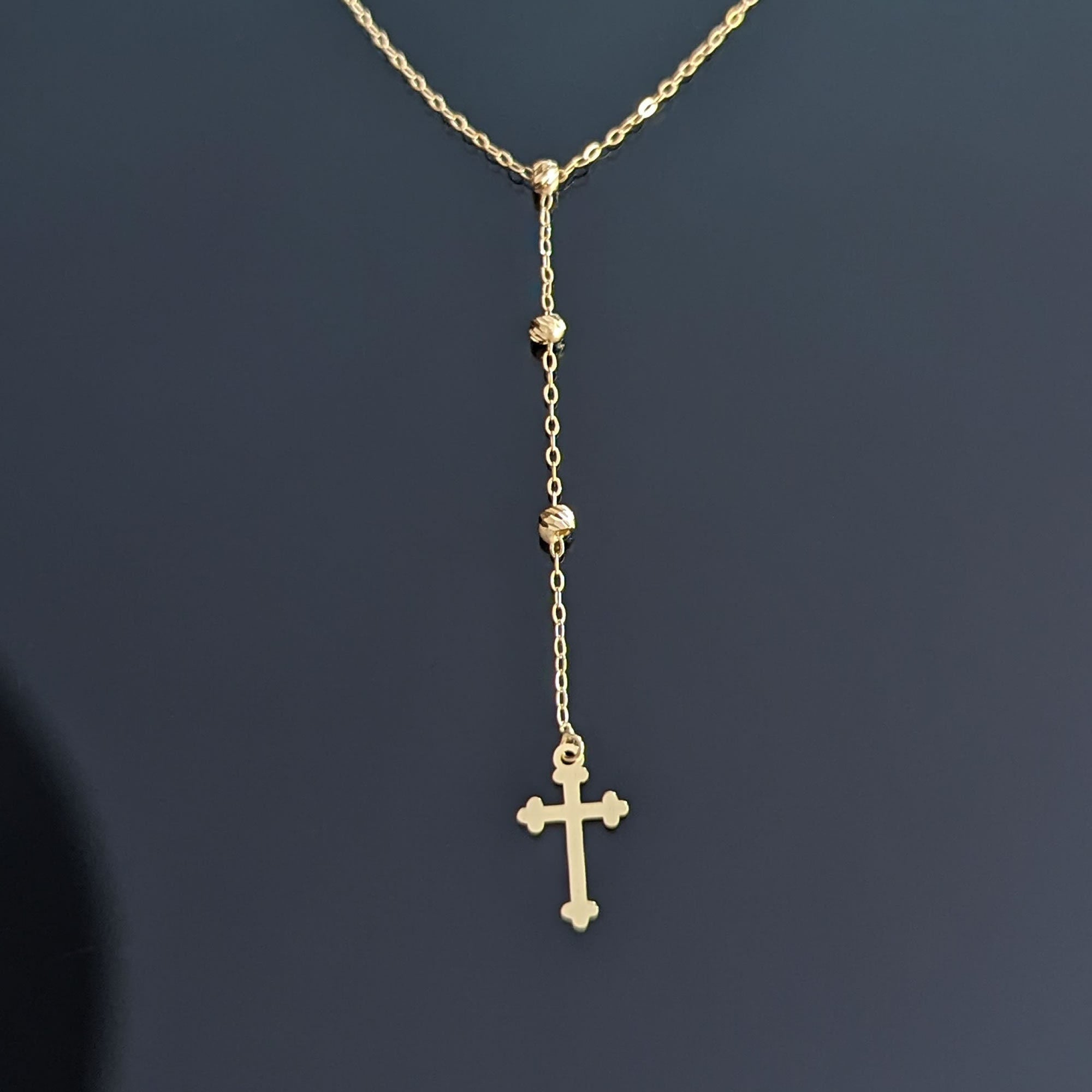 Close-up image of a 14K gold rosary-style necklace with a delicate cross pendant