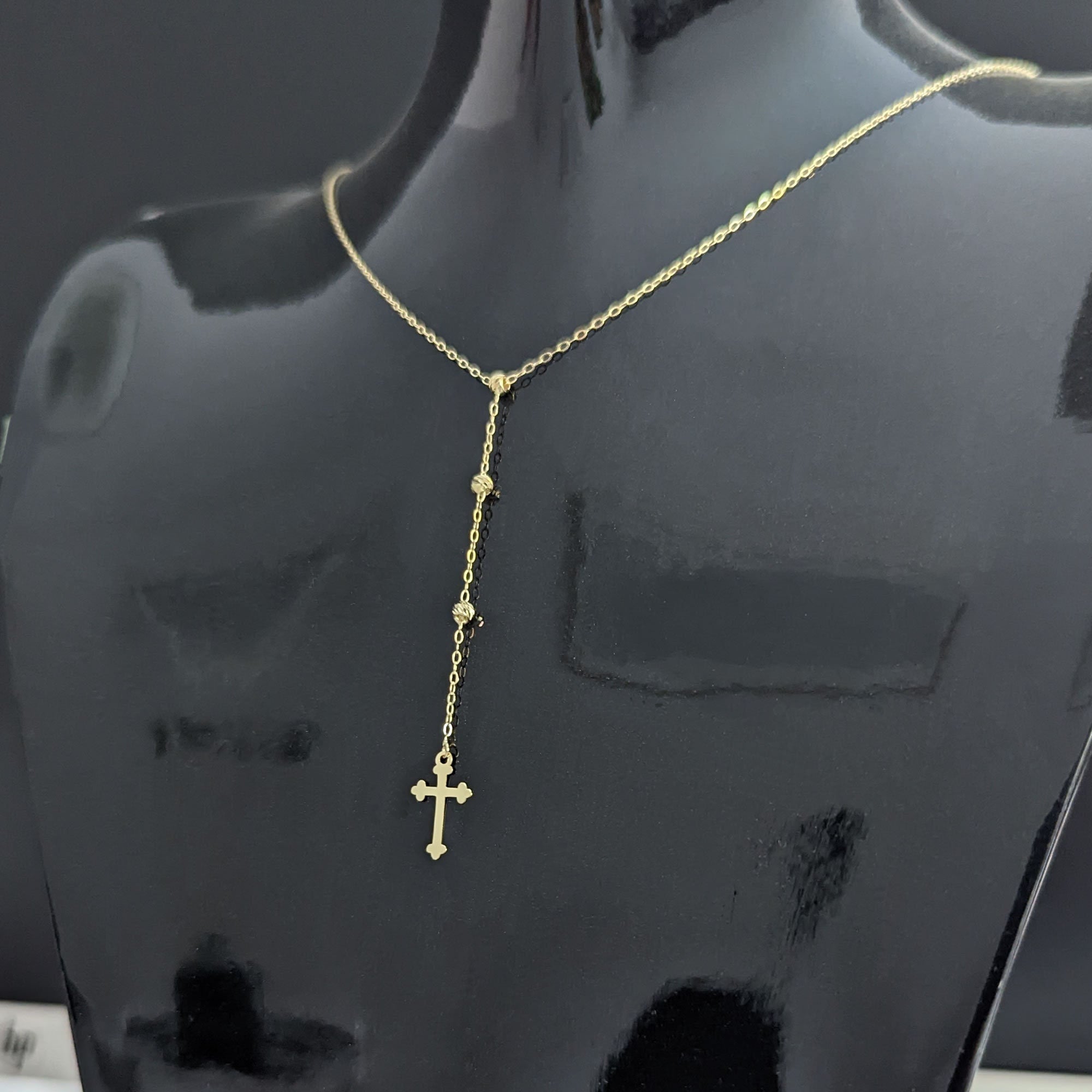 Close-up image of a 14K gold rosary-style necklace with a delicate cross pendant