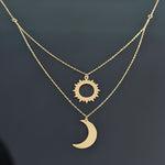 Layered 14K gold necklace with a polished crescent moon and cut-out sun pendant displayed on a dark reflective background.