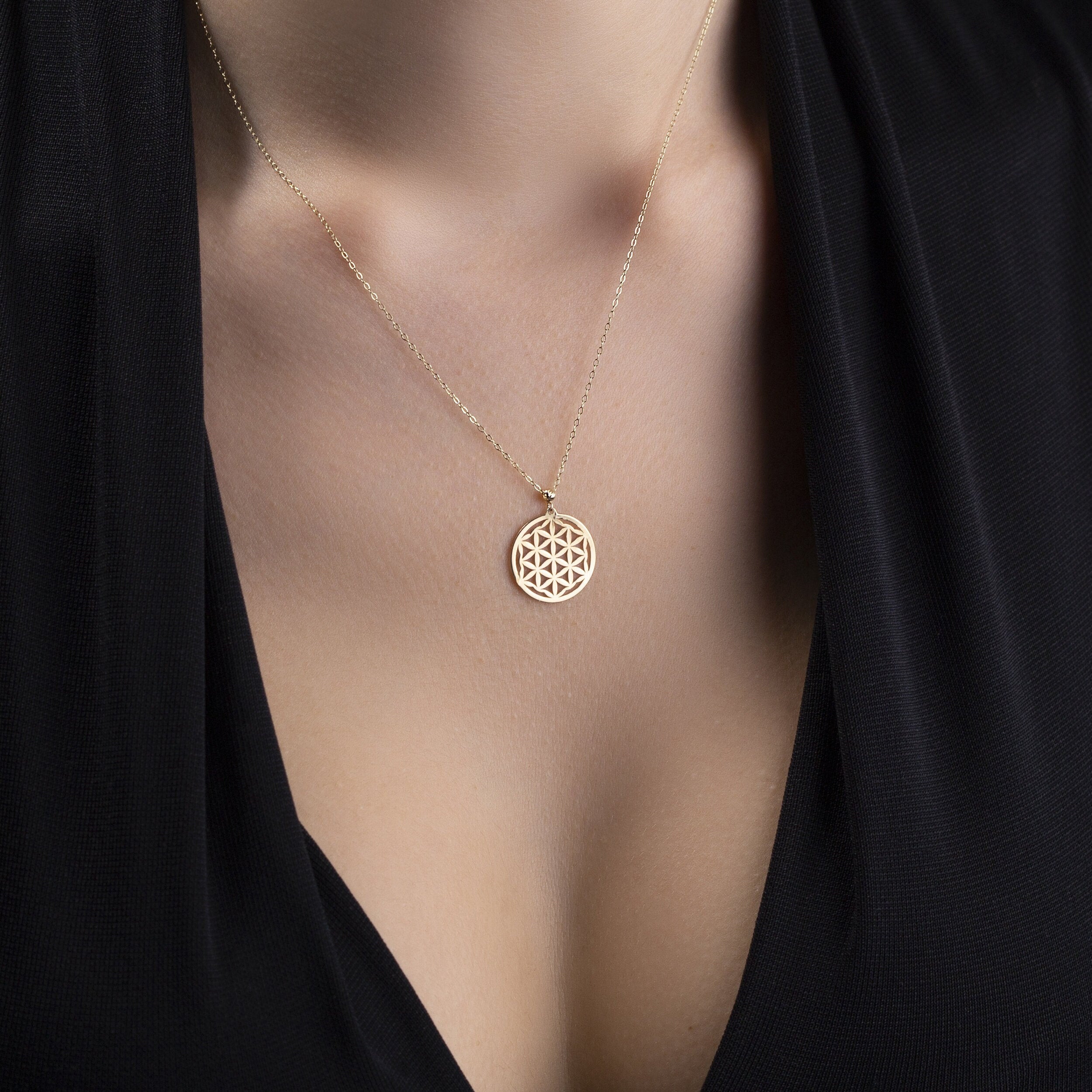 14K gold Flower of Life pendant necklace on deep purple fabric – sacred geometry jewelry with spiritual symbolism.