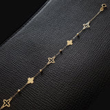 Elegant 14K gold bracelet featuring alternating solid and hollow clover charms with gold bead accents, laid on black textured leather background.
