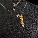 Seven-star cascade necklace in 14K gold displayed on black textured leather background, featuring minimalist celestial design.