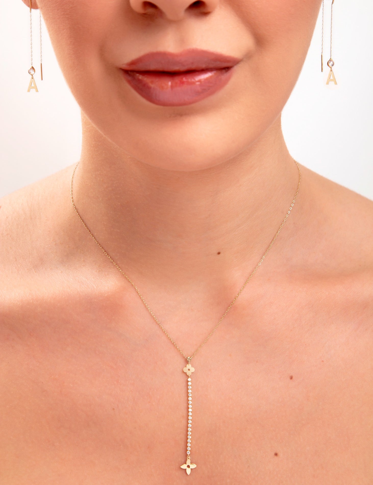 Close-up of woman wearing floral crystal drop necklace and gold initial threader earrings, featuring the letter “A”

