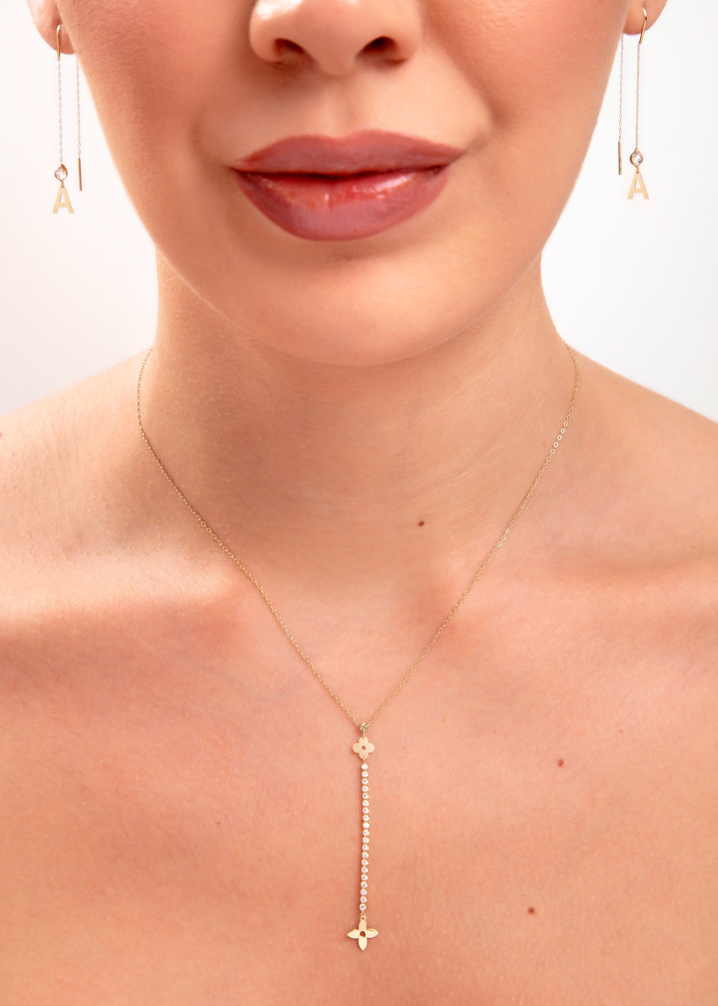 Close-up of woman wearing floral crystal drop necklace and gold initial threader earrings, featuring the letter “A”

