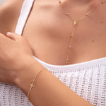 Close-up of a woman wearing a 14K gold plated rosary-style necklace with drop cross and matching cross bracelet with crystals, styled with white knitwear

